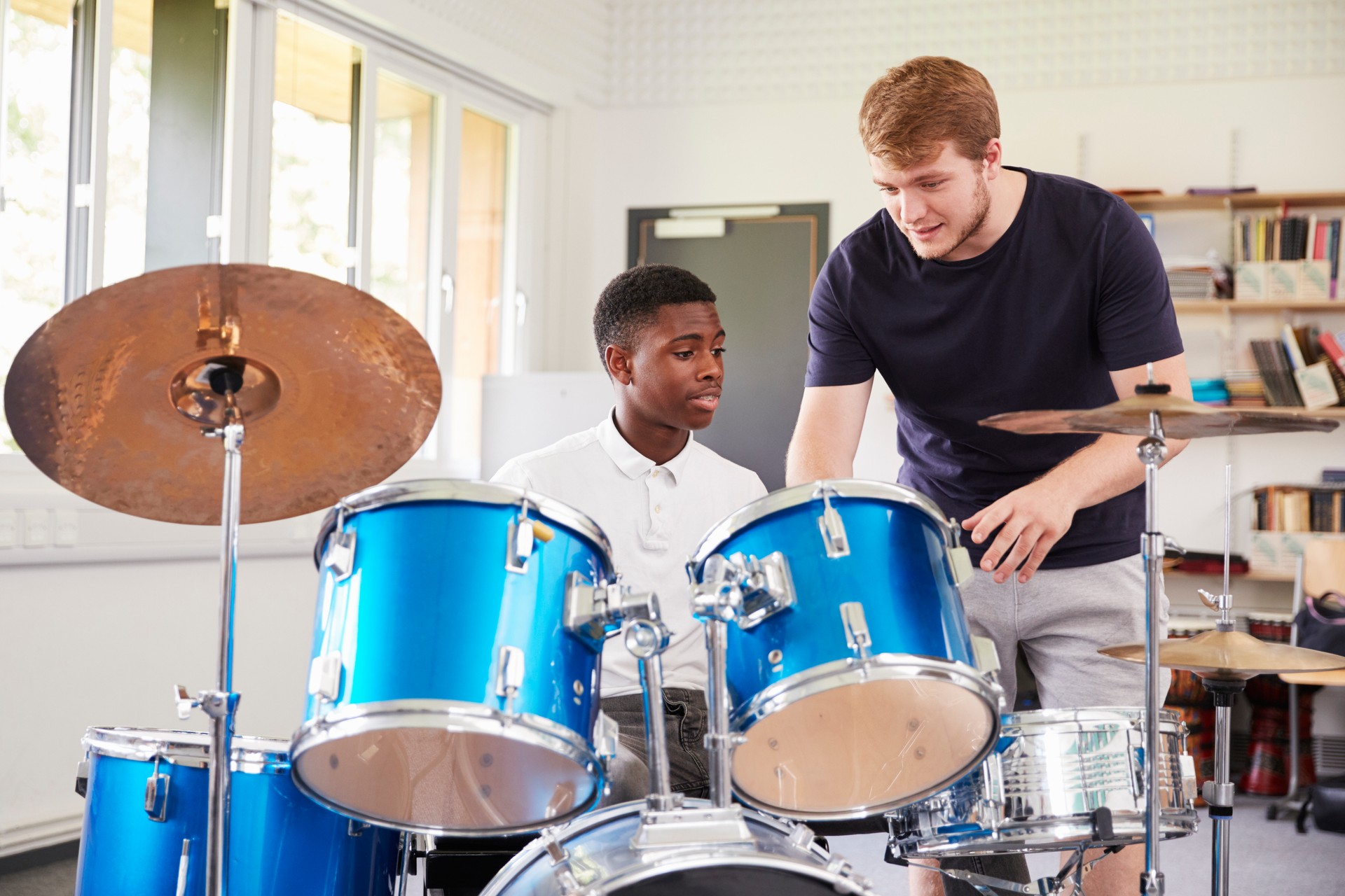 Male Pupil With Teacher Playing Drums In Music Lesson