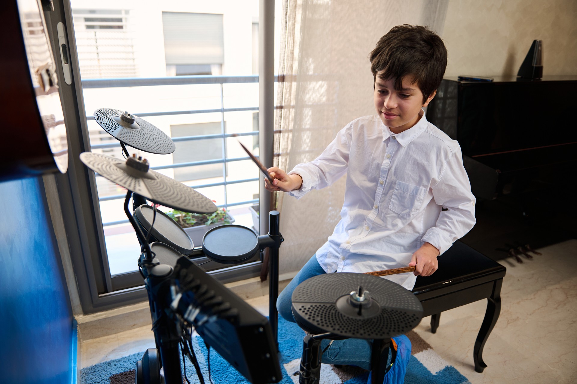 Teenager boy playing drums at home music studio, holding drumsticks and banging drums, beating on drum kit. Learning percussion musical instrument